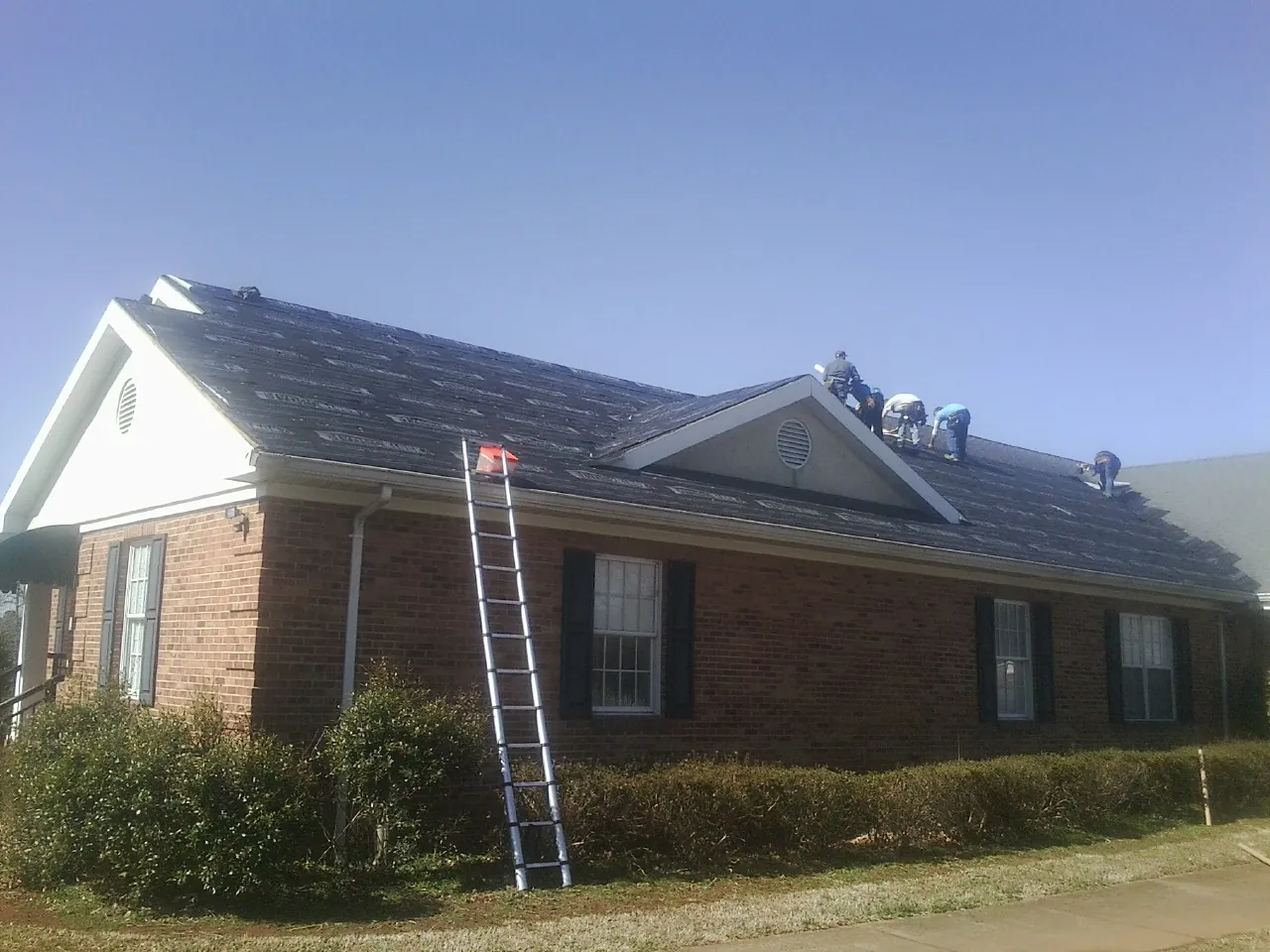Crew tearing shingles off a brick ranch roof with a ladder set — Metal Roof Repair work by our crew in Holt